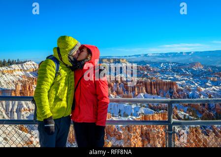 Coppia giovane kissing, punto di vista, bizzarro innevato paesaggio roccioso con Hoodoos in inverno, Sunset Point, Parco Nazionale di Bryce Canyon Foto Stock
