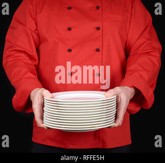 Cuocere in rosso uniforme tiene nelle sue mani una pila di bianco rotondo per le placche vuote, sfondo nero Foto Stock