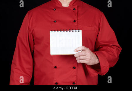 Chef in rosso uniforme tenendo un fustellato notebook, sfondo nero Foto Stock