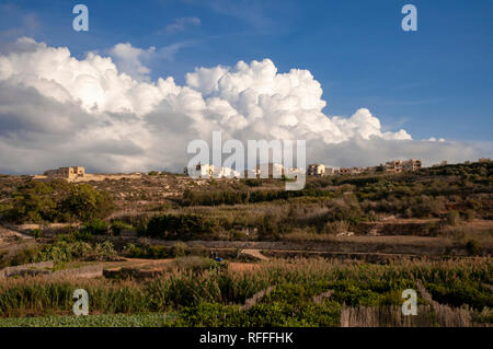 La periferia di Qala villaggio su Gozo, Malta, sotto un cielo blu con drammatica cumulus nubi edificazione. Foto Stock