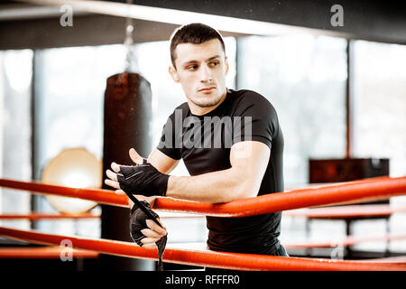 Ritratto di un giovane uomo atletico bendaggio di avvolgimento sui polsi, la preparazione per la formazione su pugilato ring in palestra Foto Stock