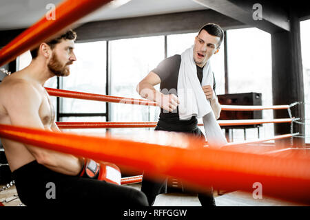 Boxing Trainer dando istruzioni durante una pausa per motivare un pugile seduto su un angolo del pugilato ring Foto Stock