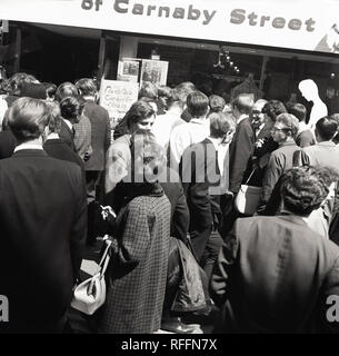 1967, storico, una folla di gente che si mescolano al di fuori di un negozio a Carnaby Street, Londra, Inghilterra, Regno Unito. In questa epoca, Carnaby Street è stata il centro del British Fashion scena con molti negozi di abbigliamento e moda modelli rendendo le apparenze. Foto Stock