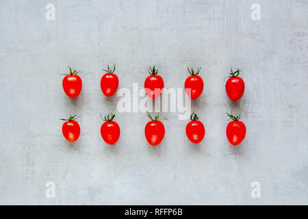 Layout creativo fatto di freschi pomodori ciliegia su uno sfondo chiaro. Cucina salutare. Concetto di cibo. Piatto, laici vista superiore Foto Stock