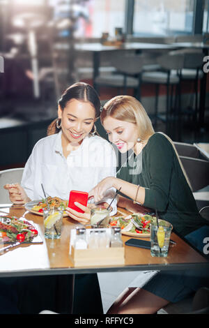 Due migliori amici newsfeed di lettura su smartphone rosso durante la cena Foto Stock