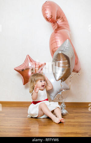 Piccola bambina bionda di due anni con grandi palloncini rosa e bianchi per  la sua festa di compleanno.