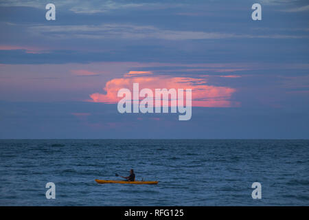 Un uomo solitario kayak di notte sullo sfondo di un bel colore rosa nuvole. Tramonto in Puerto Viejo, Costa Rica. Foto Stock