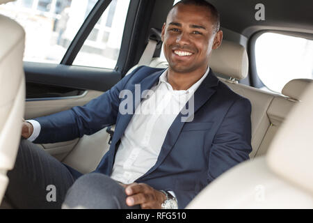 Giovane imprenditore seduto sul sedile posteriore in auto gioiosa sorridente Foto Stock