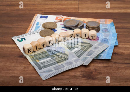 Die Euro Geldscheine und Münzen liegen auf dem Tisch mit dem Wort Elternzeit Foto Stock