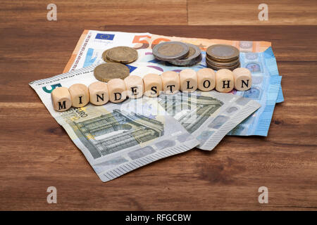 Die Euro Geldscheine und Münzen liegen auf dem Tisch mit dem Wort Mindestlohn Foto Stock