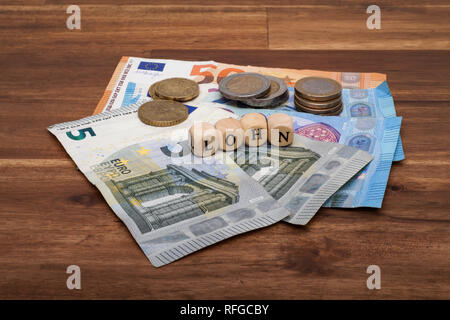 Die Euro Geldscheine und Münzen liegen auf dem Tisch mit dem Wort Lohn Foto Stock