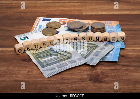 Die Euro Geldscheine und Münzen liegen auf dem Tisch mit dem Wort Grundeinkommen Foto Stock