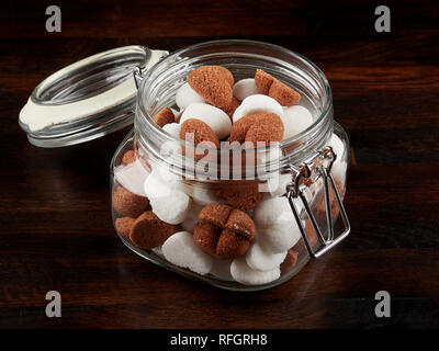 Un vaso riempito sith bianco e marrone a forma di cuore i cubetti di zucchero, al buio su un pannello di legno Foto Stock