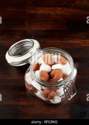 Un vaso riempito sith bianco e marrone a forma di cuore i cubetti di zucchero, al buio su un pannello di legno Foto Stock