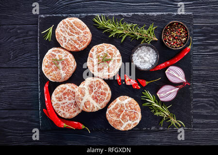 Non cotti Atriaux - La carne macinata di maiale avvolto nel lobo grasso, swiss hamburger, tipo di bratwurst, su un vassoio di ardesia con cipolla, rosmarino e sale su un tavolo di legno Foto Stock