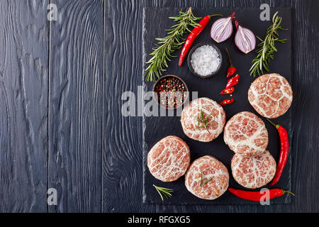 Non cotti Atriaux - La carne macinata di maiale avvolto nel lobo grasso, cucina svizzera, tipo di salsicce, hamburger su un vassoio di ardesia con rosmarino e sale su un tavolo di legno Foto Stock