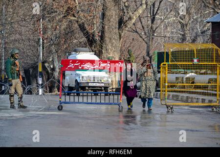 Le ragazze del Kashmir visto camminare davanti a un soldato di paramilitari di guardia al checkpoint in anticipo dell'India del giorno della Repubblica celebrazioni a Srinagar, Indiano Kashmir amministrato. La sicurezza è stata potenziata attraverso la valle del Kashmir, come lo stato è tutti insieme per celebrare il Giorno della Repubblica a Sher-e-Kashmir Stadium il 26 gennaio. Foto Stock