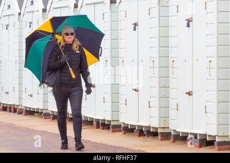 Bournemouth, Dorset, Regno Unito. 26 gennaio 2019. Tempo britannico: Una miscela di pioggia e sole a Bournemouth, come donna cammina lungo la passeggiata oltre capanne spiaggia riparando sotto un ombrello. Credit: Carolyn Jenkins/Alamy Live News Foto Stock