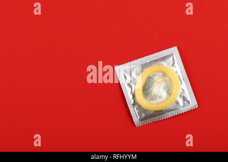 Chiudere un preservativo di lattice su argento wrap pack su vivid sfondo rosso con copia spazio, elevata angolo visuale, direttamente sopra Foto Stock