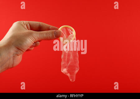 Close up man mano che tiene una aperta del condom in lattice su sfondo rosso con copia spazio, basso angolo vista laterale Foto Stock