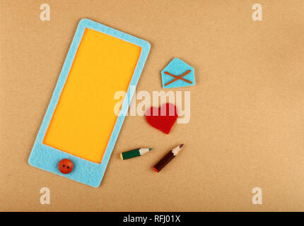 Close up feltro craft smartphone blu con giallo schermo vuoto spazio copia, il cuore e la busta posta su carta marrone di sfondo, elevati vista superiore, direc Foto Stock