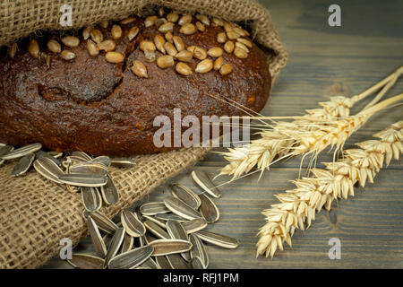 Pane con semi di girasole, orecchio di grano maturo e non sgranati Semi di girasole su tavola in legno rustico Foto Stock