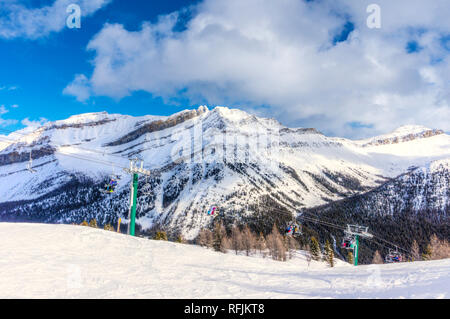 Identificabili gli sciatori e gli snowboarder sulla seggiovia andando su una pista da sci in montagna innevata gamma delle Canadian Rockies. Foto Stock