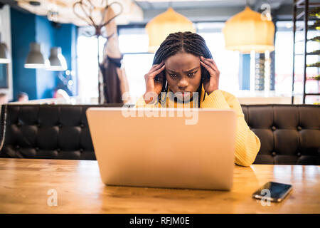 Giovane donna africana con laptop soffre di mal di testa mentre è seduto in cafe Foto Stock