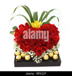 Regalo floreale disposizione realizzata con rose rosse con cioccolatini all'interno di un vaso di legno su sfondo bianco Foto Stock