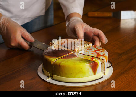 Tagli di pasticceria torta dacquoise specchiato in smalto. La cucina moderna. La donna trattiene il coltello pezzo di torta. Visto torte e ripieni. Yummy Foto Stock
