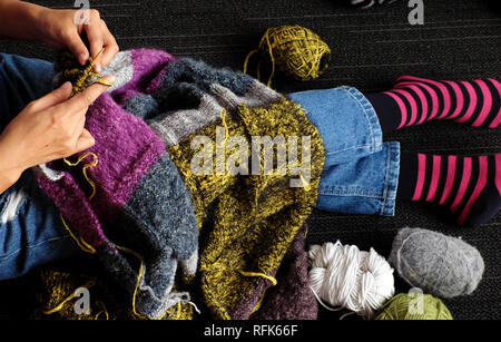 Donna asiatica sedersi sul pavimento di casa a lavorare a maglia coperta di lana per riscaldare in inverno, la maglia è un hobby in attività del tempo libero per fare dono fatti a mano, foto di Foto Stock