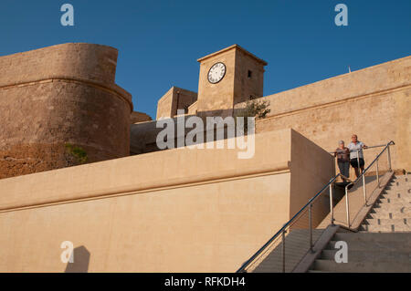 Una coppia di anziani in piedi nella zona intorno all'ingresso principale della cittadella fort in Victoria, Gozo, Malta. A sinistra su St Martin Demi-Bastion. Foto Stock