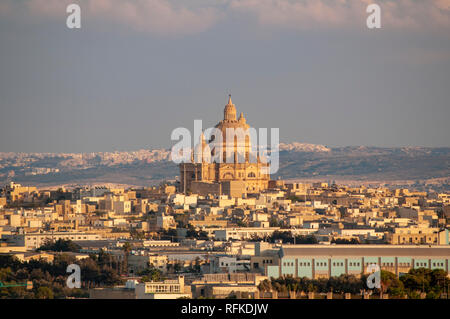 La prominente chiesa di San Giovanni Battista Seduto maestosamente nel villaggio di Xewkija a Gozo, Malta, contro lo sfondo di Ghajnsielem comune. Foto Stock