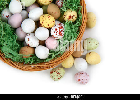 Il cioccolato mini uova di Pasqua in paglia o cesto di vimini contro uno sfondo bianco Foto Stock