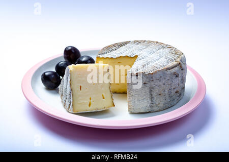 Round coppia francese di formaggio tomme con un pezzo tagliato e Fresche uve mature su una lavagna bianca isolata da vicino Foto Stock