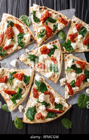 Pane appena sfornato flatbread con hummus, pomodori secchi, spinaci e formaggio di capra vicino sul tavolo. verticale in alto vista da sopra Foto Stock