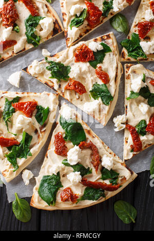 Pane appena sfornato flatbread con hummus, pomodori secchi, spinaci e formaggio di capra vicino sul tavolo. Verticale in alto vista da sopra Foto Stock