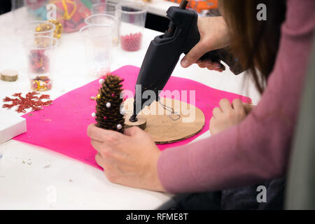 Ghirlanda di Natale atelier di tessitura. Donna mani decorazione ghirlanda di vacanza fatta di rami di abete rosso, coni e varie decorazioni organico sul tavolo Foto Stock