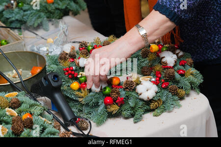 Ghirlanda di Natale atelier di tessitura. Donna mani decorazione ghirlanda di vacanza fatta di rami di abete rosso, coni e varie decorazioni organico sul tavolo Foto Stock