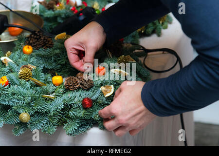 Ghirlanda di Natale atelier di tessitura. Donna mani decorazione ghirlanda di vacanza fatta di rami di abete rosso, coni e varie decorazioni organico sul tavolo Foto Stock