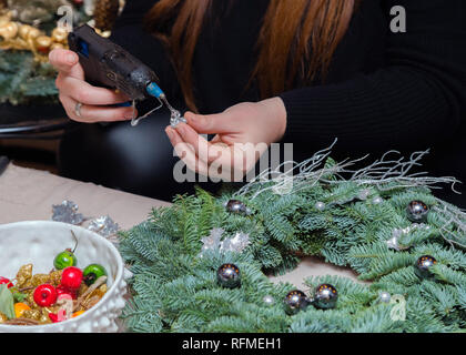 Ghirlanda di Natale atelier di tessitura. Donna mani decorazione ghirlanda di vacanza fatta di rami di abete rosso, coni e varie decorazioni organico sul tavolo Foto Stock