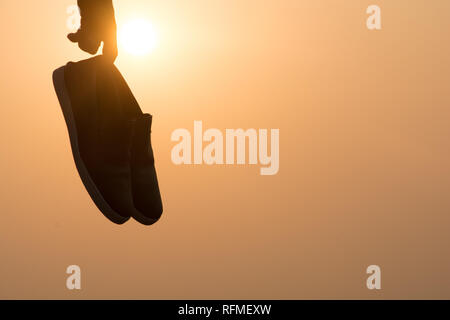 Il ragazzo che sta al tramonto e azienda di scarpe in sua mano Close-up Foto Stock