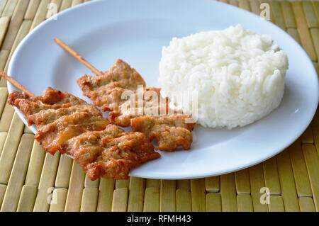 Carne di maiale alla griglia pugnalata bastone di legno mangiare giovane con riso Foto Stock