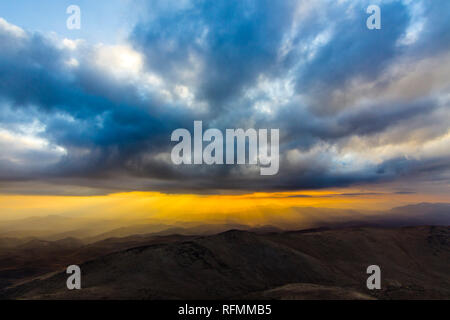 Tramonto a 'La Silla' Osservatorio, una vista al di sopra della linea di orizzonte con i raggi di luce provenienti dal sole che passa nubi strati al di sopra delle montagne Foto Stock