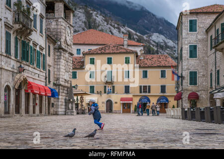 Kotor, Montenegro - Aprile 2018 : Ragazzo rincorrere i piccioni sulla piazza storica di armi nella città vecchia di Kotor, Foto Stock