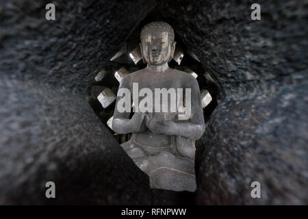 Una vista di un Buddha in uno degli stupa al tempio di Borobudur in Java, Indonesia. Foto Stock