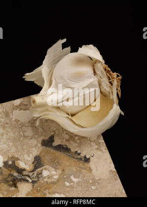 Spicchio di aglio bilanciato sul ripiano di marmo contro uno sfondo nero, alimento vegetale fotografia Foto Stock