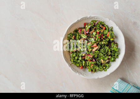 Prezzemolo tritato con insalata di pomodoro e cipolle in vaso di ceramica sulla superficie di marmo. Alimenti biologici. Foto Stock