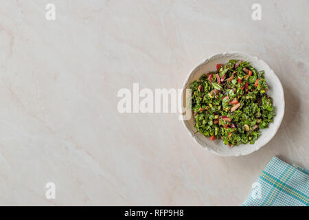 Prezzemolo tritato con insalata di pomodoro e cipolle in vaso di ceramica sulla superficie di marmo. Alimenti biologici. Foto Stock