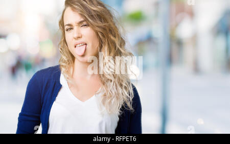 Giovane e bella donna bionda su sfondo isolato con la lingua fuori con felice espressione divertente. Concetto di emozione. Foto Stock